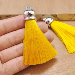 May include: Two yellow silk tassels with silver metal caps. The tassels are about 3 inches long and are held in a hand.