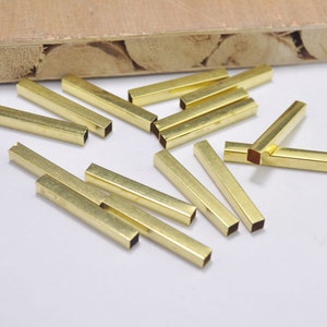 May include: A group of 16 gold-colored metal tubes, each with a square cross-section. The tubes are scattered on a light brown surface.
