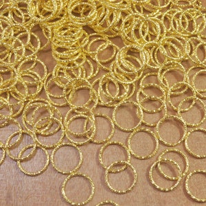 Puede incluir: Un montón grande de anillos de salto de metal de color dorado. Los anillos son todos del mismo tamaño y están dispuestos en un patrón aleatorio.