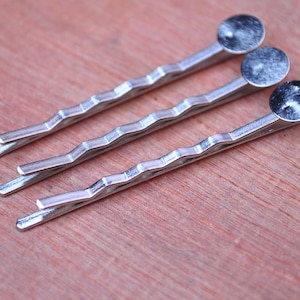 Op de afbeelding: Drie zilveren haarclips met ronde, zilverkleurige metalen uiteinden.
