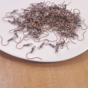 May include: A pile of copper-toned earring hooks with a spring-loaded closure. The hooks are on a white plate.