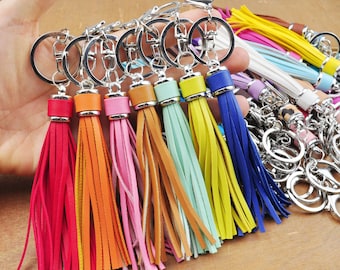 May include: A set of colorful tassel keychains with silver key rings. The tassels are made of leather and come in a variety of colors, including red, orange, yellow, green, blue, and purple.