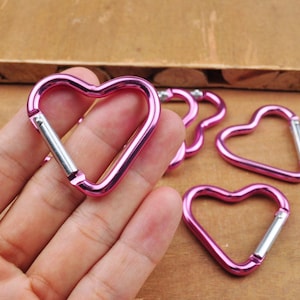 Pode incluir: Cinco chaveiros de metal em forma de coração rosa com um fecho de mola prateado.