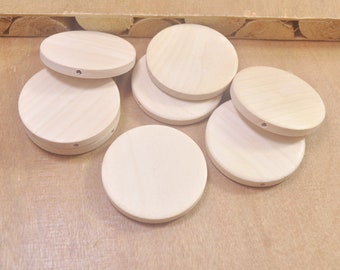 May include: Six unfinished wooden circles with a small hole in the center. The circles are arranged in a semi-circle on a light brown surface.