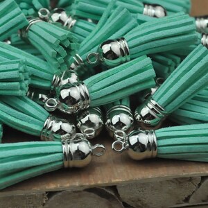 May include: A pile of teal blue suede tassels with silver metal caps. The tassels are arranged in a random pattern and are all the same size.