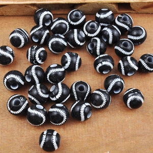 May include: A collection of black and white baseball-themed beads. The beads are round and have a white stitching design.