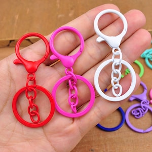 May include: Three metal keychains with different colored rings and chains. The keychains are pink, red, and white.