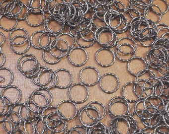 May include: A close-up of a pile of silver-coloured metal rings. The rings are all different sizes and shapes, and they are arranged in a random pattern.
