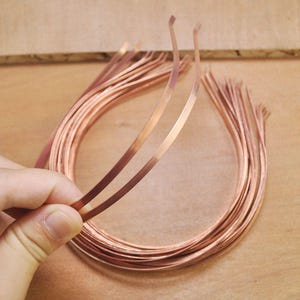 Peut inclure: Une pile de bandeaux de tête en métal de couleur cuivre, chacun d'environ 1,2 cm de large. Les bandeaux sont pliés en forme de cercle et sont empilés les uns sur les autres.