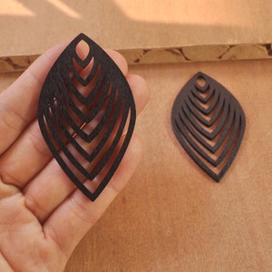 May include: Two black wooden leaf-shaped earrings with a layered, geometric design. Each earring has a small hole at the top for hanging.