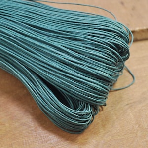 Può includere: Cordoncino di cotone cerato blu turchese, un tipo di spago, avvolto in una bobina. Il cordoncino è liscio e ha una lucentezza sottile.