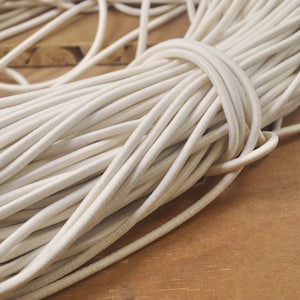 May include: A close-up of a large bundle of white elastic cord. The cord is tightly wound and appears to be made of a soft, flexible material.
