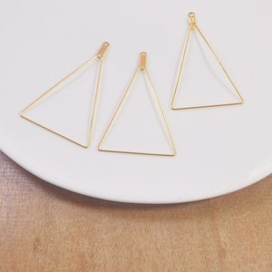 May include: Three gold triangle shaped wire hoops on a white plate. The hoops are about 2 inches in diameter.