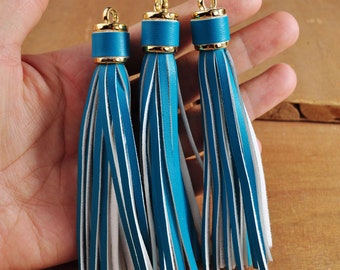 May include: Three teal blue leather tassels with white accents and gold metal tops.