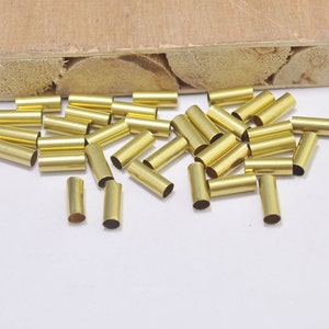 May include: A group of gold-colored metal tubes, scattered on a white surface. The tubes are about 1 inch long and have a smooth, shiny finish.