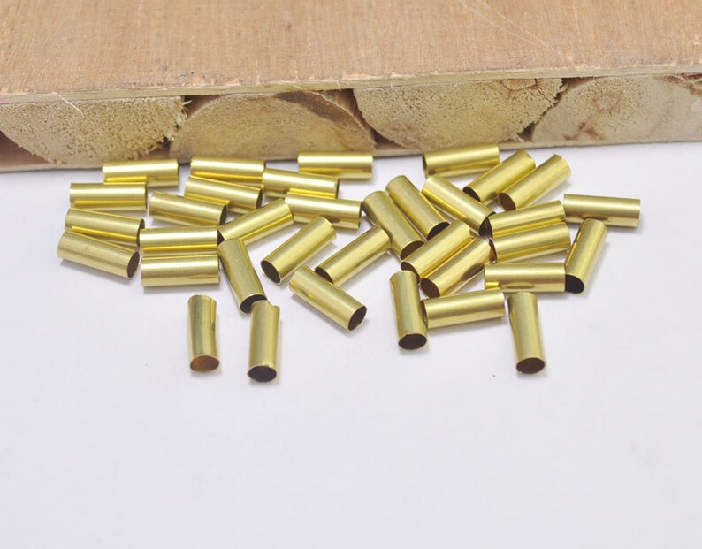 May include: A group of gold-colored metal tubes, scattered on a white surface. The tubes are about 1 inch long and have a smooth, shiny finish.