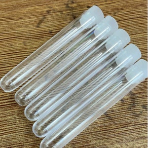 May include: A set of six clear glass test tubes with white plastic caps. The test tubes are arranged in a row, with the caps facing the viewer.