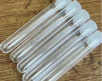 Puede incluir: Un juego de seis tubos de ensayo de vidrio transparente con tapas de plástico blanco. Los tubos de ensayo están dispuestos en una fila, con las tapas mirando al espectador.