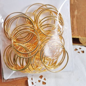 May include: A clear plastic bag filled with a large quantity of gold-colored metal jump rings. The rings are of various sizes and are arranged in a random pattern.