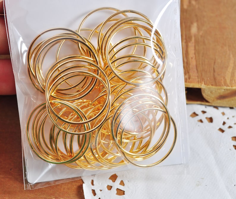 May include: A clear plastic bag filled with a large quantity of gold-colored metal jump rings. The rings are of various sizes and are arranged in a random pattern.