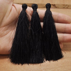 May include: Three black tassel trim embellishments. The tassels are long and fluffy.
