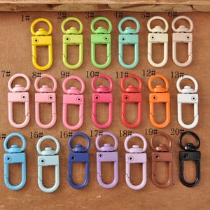 May include: A collection of colorful metal swivel clasps in various shades, including yellow, green, blue, pink, and orange. Each clasp has a D-ring and a swivel hook, perfect for attaching to keychains or bags.