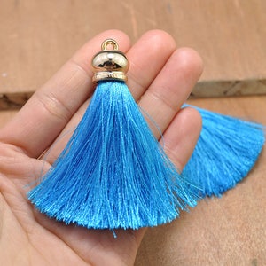 Peut inclure: Deux pompons en soie bleu vif avec des embouts en métal doré. Les pompons sont doux et moelleux, et ils seraient parfaits pour ajouter une touche d'élégance à tout projet.