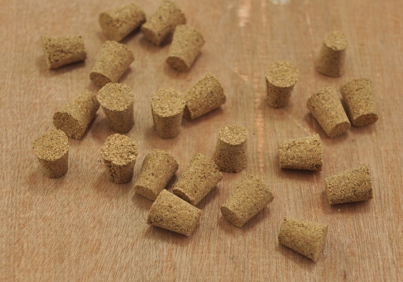 May include: A collection of brown cork bottle stoppers of various sizes. The stoppers are scattered on a light brown wooden surface.