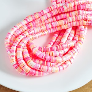 以下が含まれることがあります： ピンク、白、オレンジの丸いセラミックビーズのストランドのクローズアップ。ビーズは互いに積み重ねられており、レイヤー効果を生み出しています。