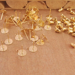 May include: A collection of gold-toned earring findings, including earring posts with flat backs, earring posts with loops, and earring backs.