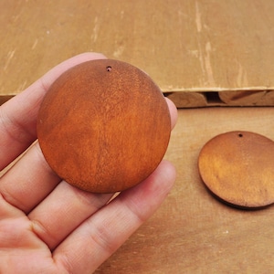 May include: Two round wooden craft blanks with a hole in the top. The blanks are a light brown colour and have a smooth finish.