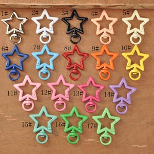 May include: A collection of seventeen star-shaped swivel clasps in various colors, including silver, white, black, peach, cream, blue, light blue, red, orange, yellow, pink, and green. Each clasp has a metal ring for attaching to items.