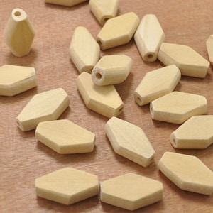 May include: A group of wooden beads in a light beige color. The beads are shaped like a hexagon with rounded edges. The beads are scattered on a wooden surface.