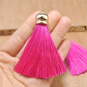 May include: A bright pink tassel with a gold metal top. The tassel is made of soft, silky threads and is approximately 2 inches long.