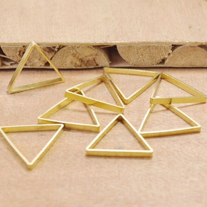 May include: A group of eight gold-colored triangle-shaped metal rings. The rings are arranged in a loose pile on a light brown wooden surface.