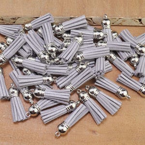 May include: A pile of silver tassel trim with a grey suede finish. The tassels are approximately 1 inch long and have a silver metal loop at the top.