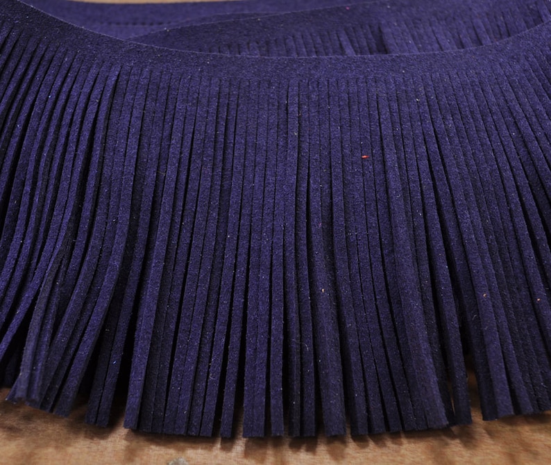 May include: A close-up of a dark purple fringe trim. The fringe is made of soft, thin strands of fabric.