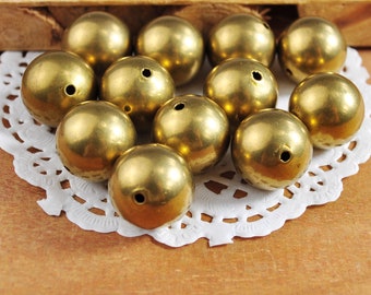 May include: A group of 10 gold-colored metal beads with a hole in the center of each bead. The beads are arranged in a pile on a white doily.