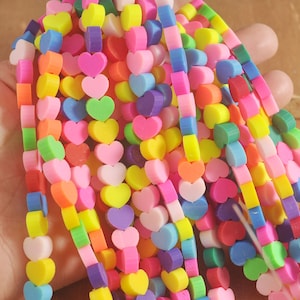 Pode incluir: Um fio colorido de contas em forma de coração em vários tons de rosa, vermelho, laranja, amarelo, verde, azul e roxo. As contas são enfiadas em um cordão elástico transparente.