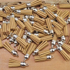 May include: A pile of brown suede tassels with silver metal caps. The tassels are all the same size and shape, and they are arranged in a random pattern.
