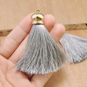 May include: A gray tassel with a gold metal top. The tassel is made of soft, silky threads and is approximately 2 inches long.