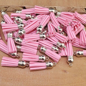 May include: A pile of pink suede tassels with silver metal caps. The tassels are approximately 2.5 cm long.