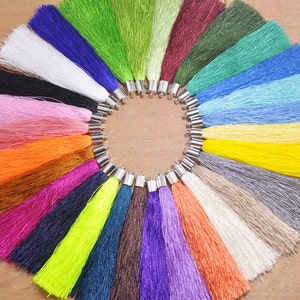May include: A collection of 20 colorful tassels with silver metal caps. The tassels are arranged in a circle on a wooden surface.