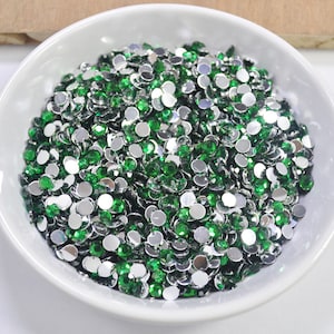 Op de afbeelding: Een kom gevuld met groene en zilveren ronde strass steentjes. De strass steentjes zijn klein en hebben een platte achterkant.
