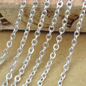 Puede incluir: Varias hebras de cadena plateada, dispuestas en fila sobre una superficie de madera. Las cadenas están hechas de pequeños eslabones redondos.