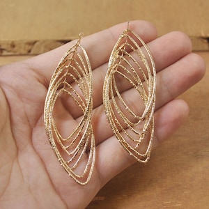 May include: A pair of gold-tone dangle earrings with a layered oval design. The earrings are made of thin, delicate wire and have a slightly textured finish.