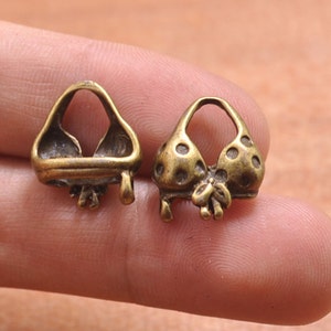 May include: Two gold-toned metal charms shaped like a bikini top. One charm has a polka dot pattern and the other is plain.