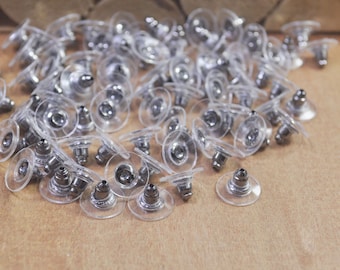 May include: A pile of clear plastic earring backs with silver metal posts. The backs are designed to be used with stud earrings.