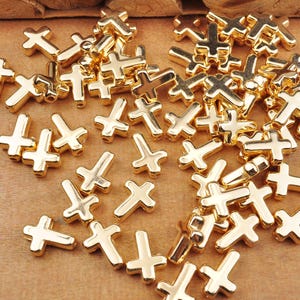 Könnte beinhalten: Ein großer Haufen goldfarbener Metallkreuz-Anhänger. Die Anhänger sind auf einer Holzoberfläche verstreut.
