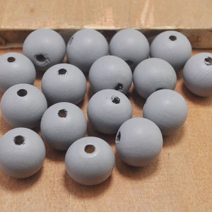 Puede incluir: Un montón de 15 cuentas de madera grises con un agujero en el centro de cada cuenta. Las cuentas están esparcidas sobre una superficie de madera marrón claro.